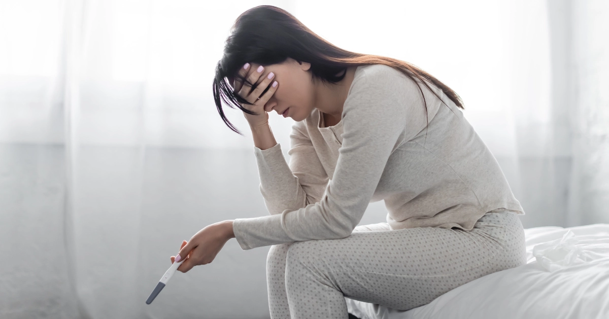 A teen holding a pregnancy test in her bed.