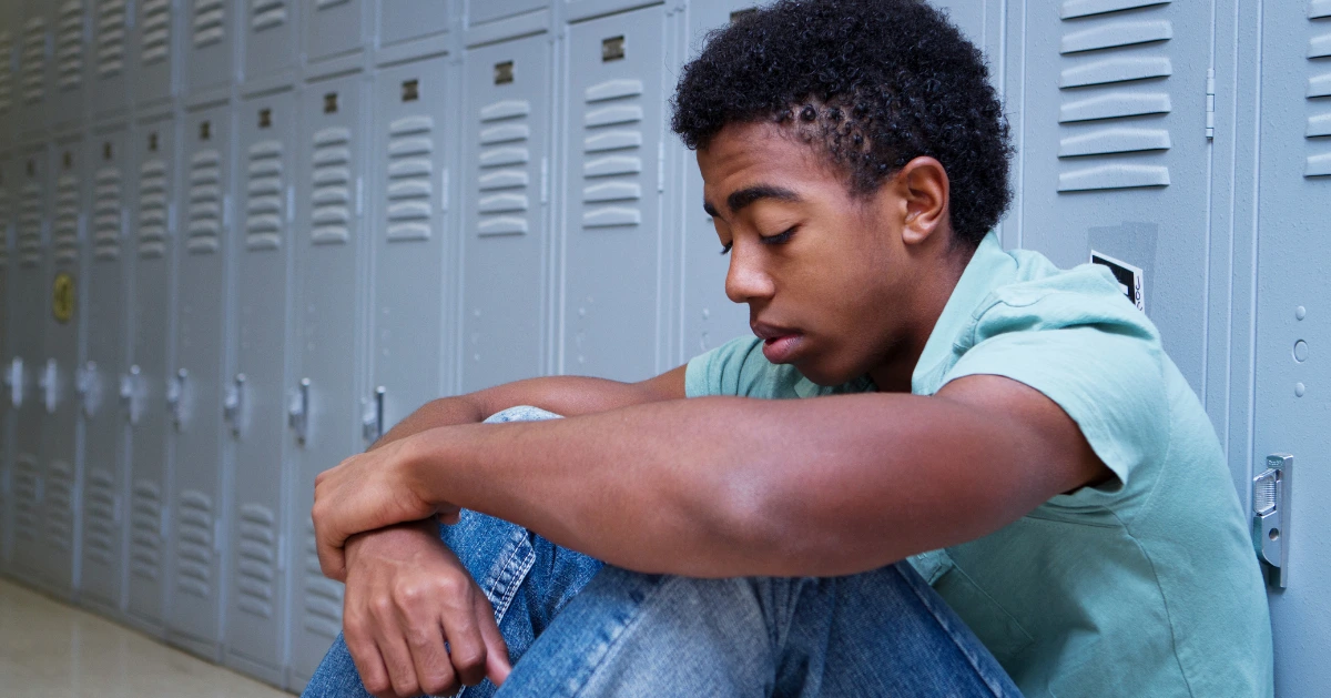 a teen sitting on the floor at school looking depressed